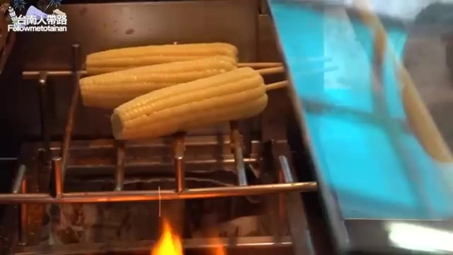 不鏽鋼烤架上正在烘烤數支玉米,底下爐火燃燒