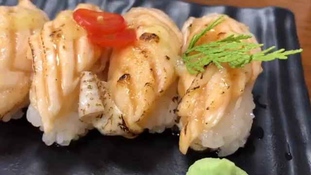 黑色石盤上盛著炙燒鮭魚握壽司,表面帶著烤製焦香,佐以紅辣椒絲與山葵