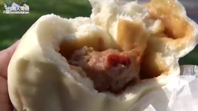 剖開的包子露出裡面的肉丸子內餡，可見紅色辣椒點綴，醬色滲入麵皮