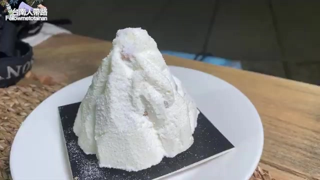 白色圓盤上擺著雪山造型的白色甜點,表面撒著糖粉,質地綿密