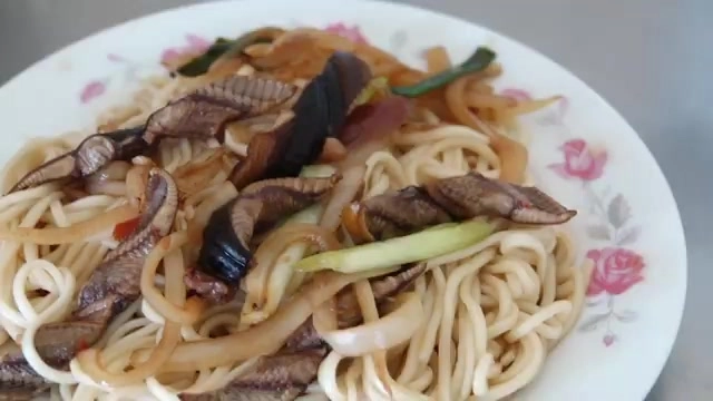 盤中盛滿炒鱔魚拌麵,鱔魚片與蔥段、洋蔥絲點綴其中,麵條油亮
