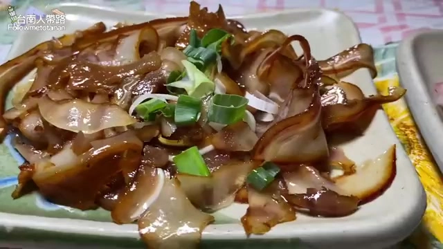 白色瓷盤中盛著切片的燒肉，撒上蔥花與洋蔥絲，醬色油亮