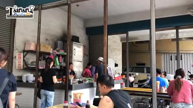 店內用餐區有多位客人正在排隊點餐與用餐,店家在後方廚房忙碌準備