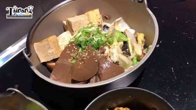 黑色鍋內盛裝多種食材,可見豆腐、鴨血、玉米、白菜與蔥花點綴,色澤豐富