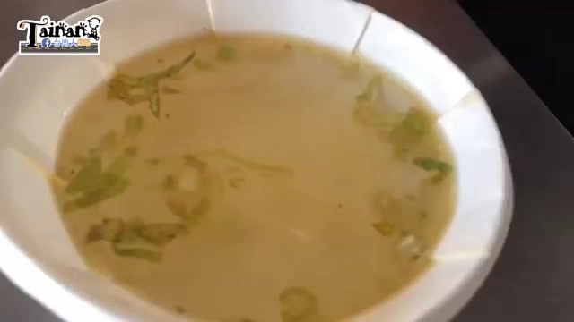 白碗中盛著淡黃色湯頭，撒上蔥花，湯色濃郁