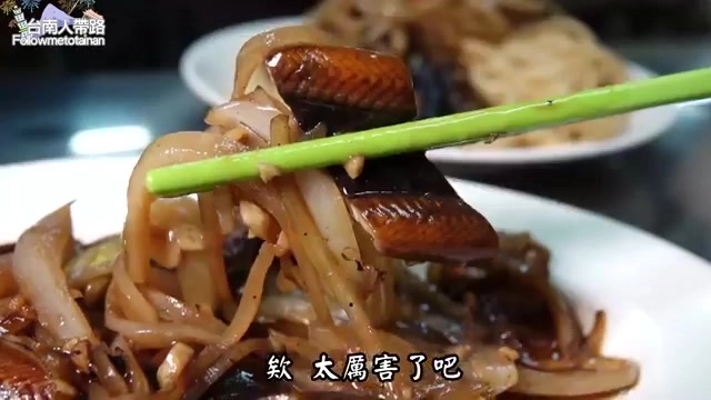 筷子夾起炒鱔魚,油亮的鱔魚肉片搭配洋蔥與麵條,醬色濃郁