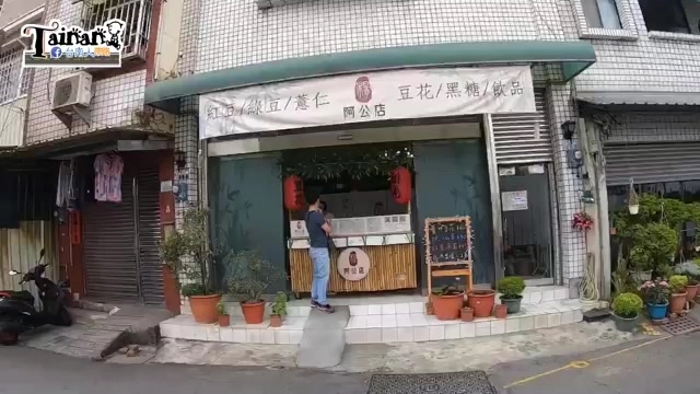 店面外觀，遮陽棚下掛著手寫菜單，寫著紅豆、綠豆、薏仁、豆花、黑糖、飲品等品項，店家招牌寫著「阿公店」，門口擺放盆栽與紅色燈籠