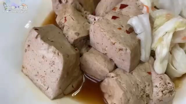 白色瓷盤中盛著切塊的蒸豆腐，色澤呈粉色，搭配新鮮泡菜點綴