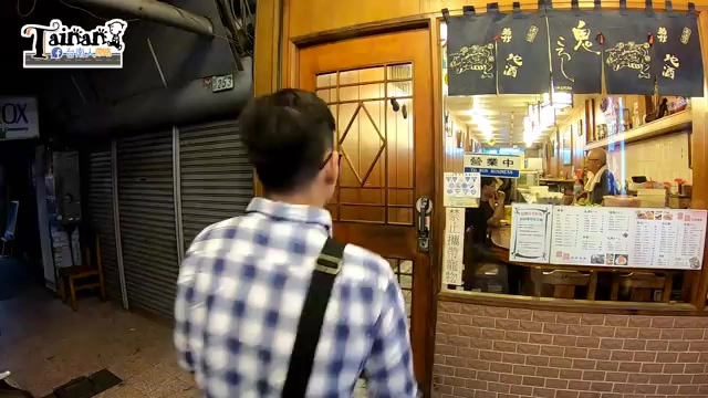 店門口掛著日式暖簾，上頭寫著壽司、こうし字樣，店內可見料理台與菜單看板，顧客背影走向店門