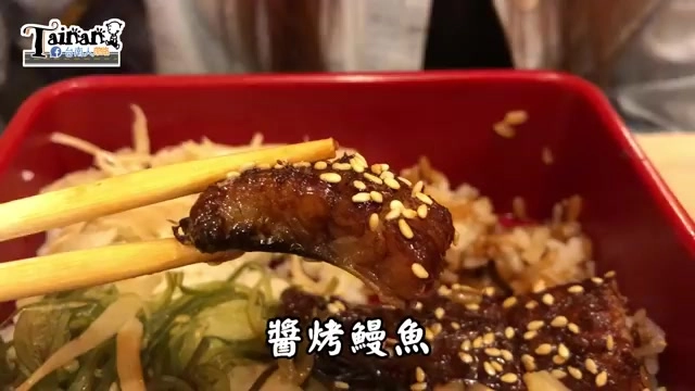 紅色餐盒盛裝醬烤鰻魚飯，鰻魚表面撒上白芝麻，一旁鋪著薑絲與海帶絲配菜
