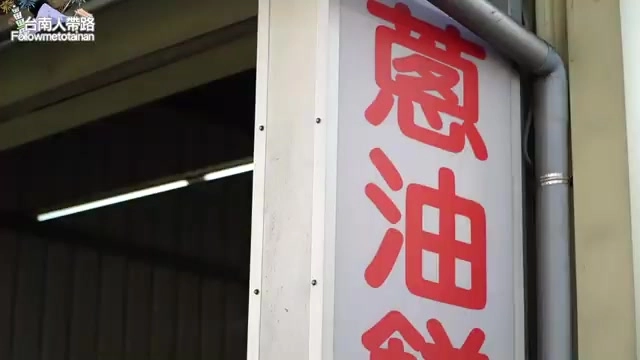 白色招牌貼在牆上,紅字寫著「蔥油餅」