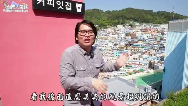 阿波在甘川洞文化村階梯前，展示身後藍黃橘交錯的繽紛階梯屋景色