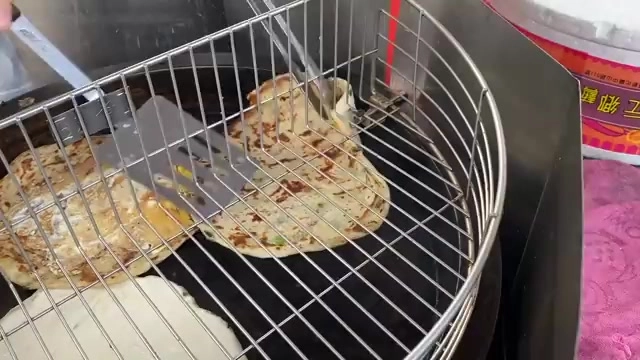 不鏽鋼烤盤上正在煎製的多張蔥抓餅，鍋鏟正翻動一張餅皮