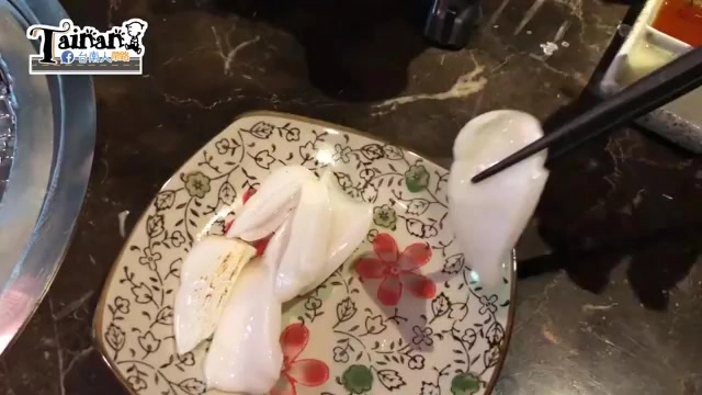 花紋瓷盤上擺著幾片生食級花枝，色澤白皙半透明，筷子夾起一片，旁邊放著沾醬