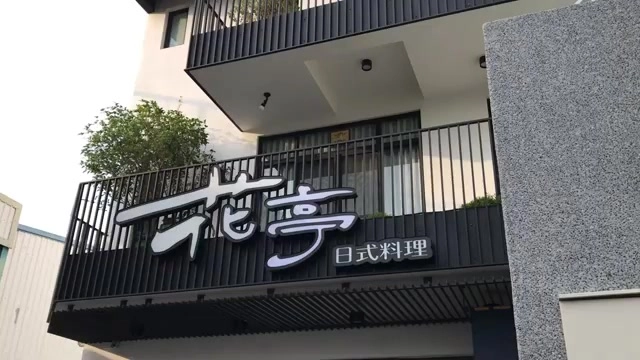 店面招牌白底黑字寫著「花亭 日式料理」，位於現代化建築外牆，二樓陽台鐵欄杆圍繞