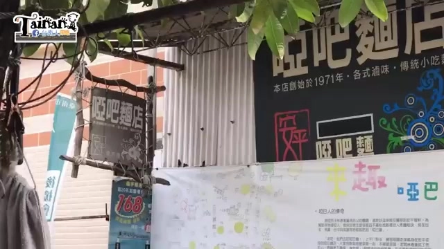 啞巴麵店的直立招牌立在窄巷轉角,招牌上寫著店名,旁邊掛著手寫菜單與紅色布條