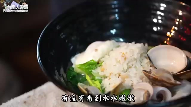 黑碗海鮮粥裡可見蛤蜊、蔬菜與米粒，粥體濕潤，賣相誘人