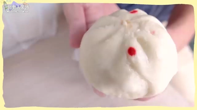 手持圓潤飽滿的白色包子,頂端點綴兩顆紅色小圓點作為口味標記