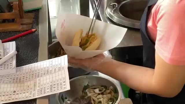 店員手持紙袋,正將夾好肉餡與香菜的餅皮裝袋,桌上擺著點餐單