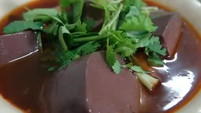 白盤中盛著深紅色的麻辣鴨血與豆腐塊,鋪滿新鮮香菜,湯汁濃稠油亮