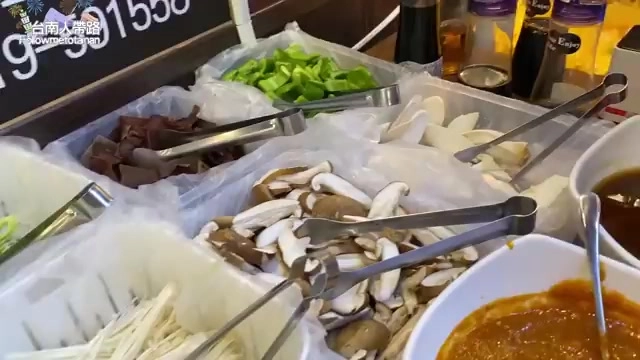 開放式自助餐台上陳列著多種火鍋料與蔬菜,包含各式菇類、豆皮、蔬菜等,用夾子方便顧客自取