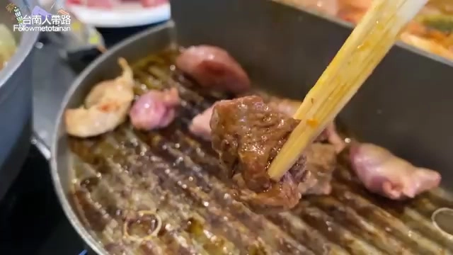 鐵板燒烤盤上正在烤製多塊牛肉與雞心,筷子夾起一塊焦香牛肉塊,油脂滋滋作響