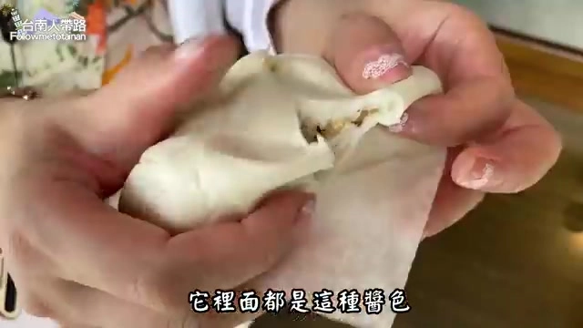 雙手撕開的包子露出深色醬汁滲入麵皮的痕跡