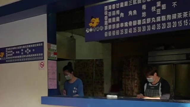 店家點餐窗口貼著藍底菜單，寫著各式炸物與甜不辣品項及價格，兩位戴口罩的店員正在裡面準備餐點