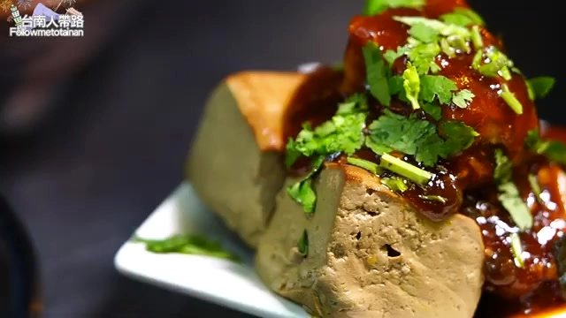 白色方盤裡盛著切塊的豆腐,淋上紅褐色醬汁並撒上香菜點綴