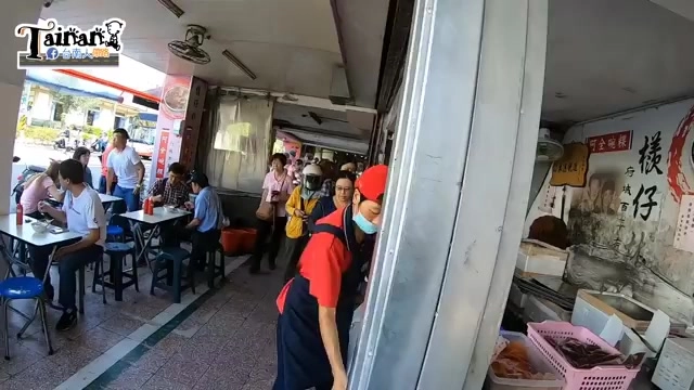 店家門口排隊人潮，桌椅擺放在騎樓下，店員穿著紅黑制服招呼顧客，一旁招牌可見「檨仔」字樣