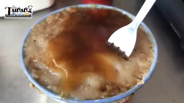 白色瓷碗盛著碗粿，表面淋著深褐色醬汁，白色湯匙插在碗中，碗粿呈現米白帶醬色的斑駁色澤