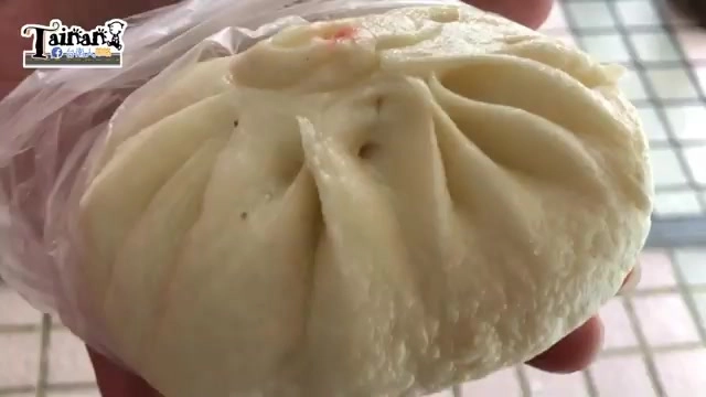 手裡拿著一顆包子，表皮呈現摺痕，頂端有紅點標記