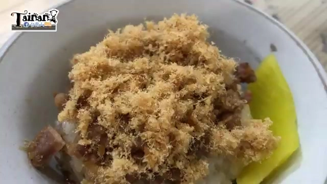 白色瓷碗盛著米糕，上面鋪滿金黃色魚鬆與肉燥，旁邊擺著醃黃瓜切片