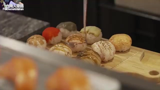 木砧板上擺著多顆握壽司，正淋上醬汁，配料豐富色澤誘人