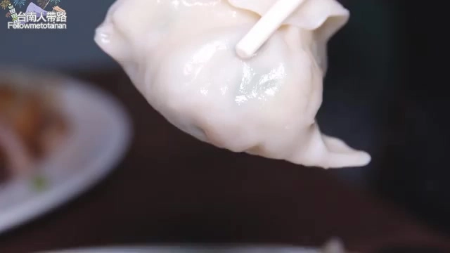 筷子夾起的整顆水餃，麵皮透亮飽滿，可見內餡輪廓