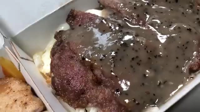 外帶餐盒中盛著牛排淋上黑胡椒醬汁，肉質切面呈現深褐色
