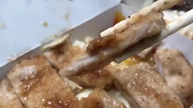 筷子夾起裹著醬汁的炸豬排，切面可見肉質紋理，色澤金黃