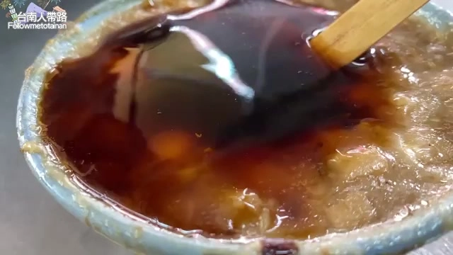 碗中盛著碗粿，淋上濃稠的深色醬汁，木棒攪拌其中