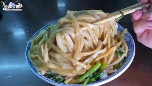 筷子夾起滿滿一大把麵條，湯汁油亮，搭配蔥花與香菜點綴