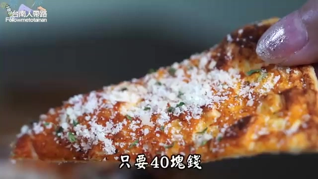 手指捏著一片披薩,表面撒滿起司粉與香料,邊緣烤得金黃酥脆,標示只要40塊錢