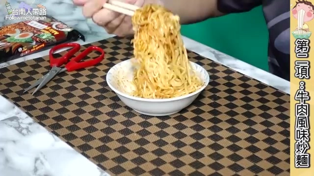 筷子高高挑起金黃色炒麵條，桌上擺著紅色剪刀與泡麵包裝袋