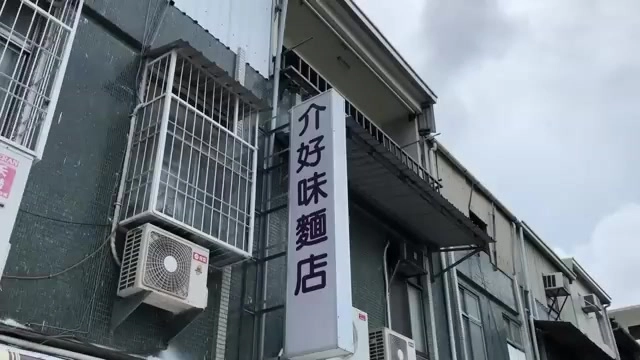 白底黑字直式招牌上寫著「介好味 麵店」，掛在建築外牆