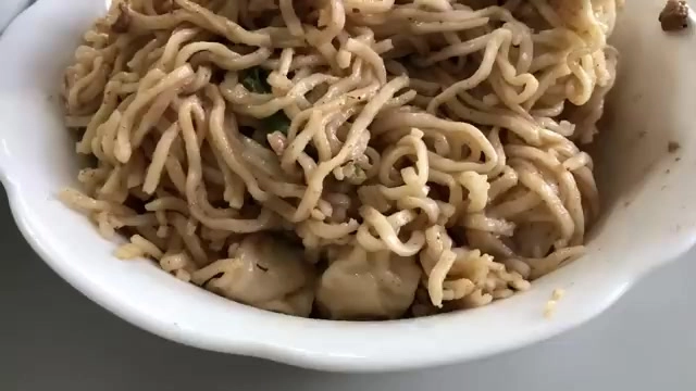 白色花邊瓷碗盛著淋上麻醬的拌麵，麵條均勻裹著醬色，點綴蔥花