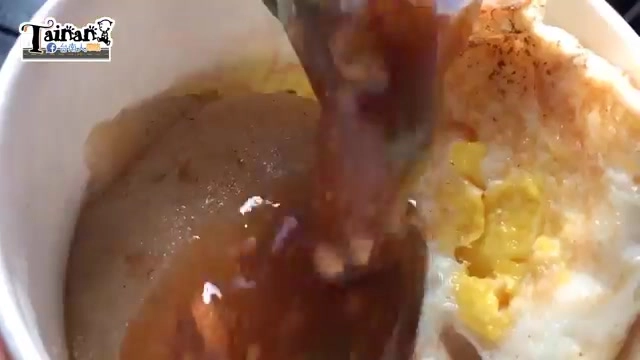 湯匙舀起濃稠的褐色醬汁淋在煎蛋與肉粿上，色澤深厚