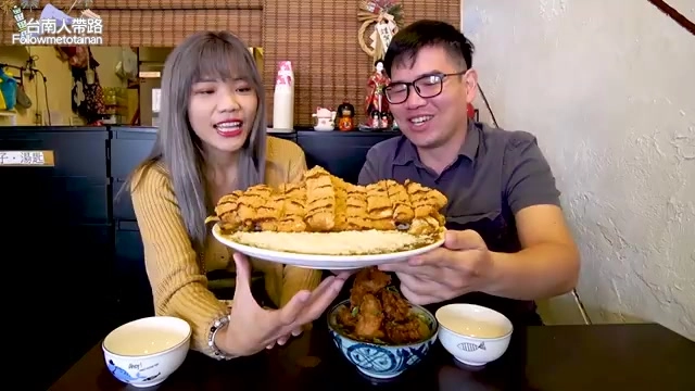 女生與男生一同端著巨大豬排拼盤,盤子幾乎與兩人臉部同寬,旁邊擺著唐揚雞丼飯與湯碗