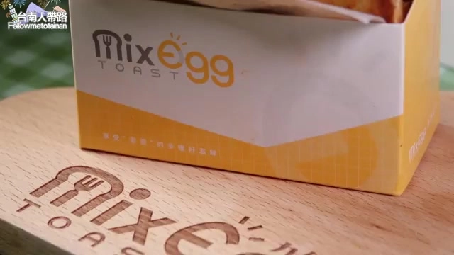 特寫拍攝黃色包裝盒，正面印著「Mix Egg TOAST」品牌字樣，放在木製托盤上