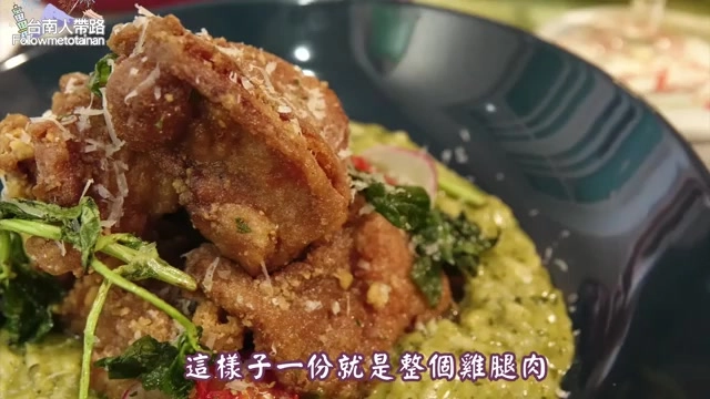 深綠色餐盤中盛著炸雞塊堆疊在青醬上，撒上起司粉與新鮮綠葉點綴