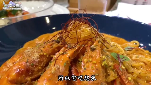 深藍色圓盤中盛著義大利麵搭配數隻大蝦，淋上橙紅色醬汁並以糖絲裝飾