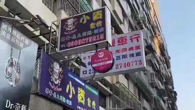 紫色與粉紅色招牌懸掛在建築外牆,寫著「小資食代」與義大利麵、燉飯等字樣