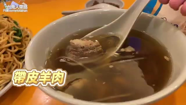 白色湯碗中盛著清澈羊肉湯,湯匙舀起一塊帶皮羊肉,色澤誘人